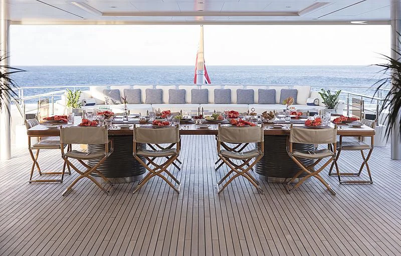 a group of tables and chairs on a deck overlooking a beach aboard ROMEA Yacht for Sale