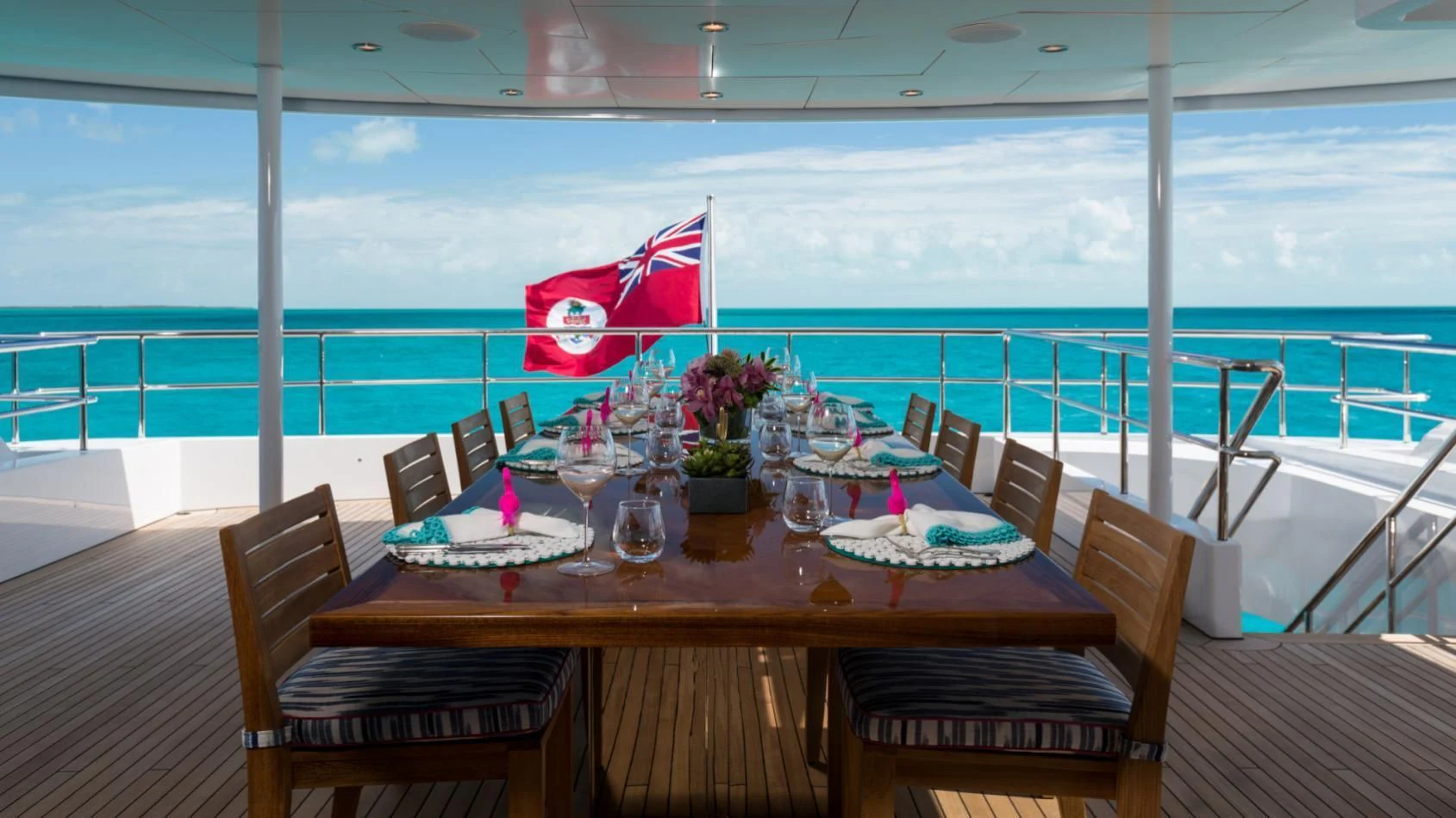 a table set with chairs and a flag on a balcony overlooking a body of water aboard BACA Yacht for Charter