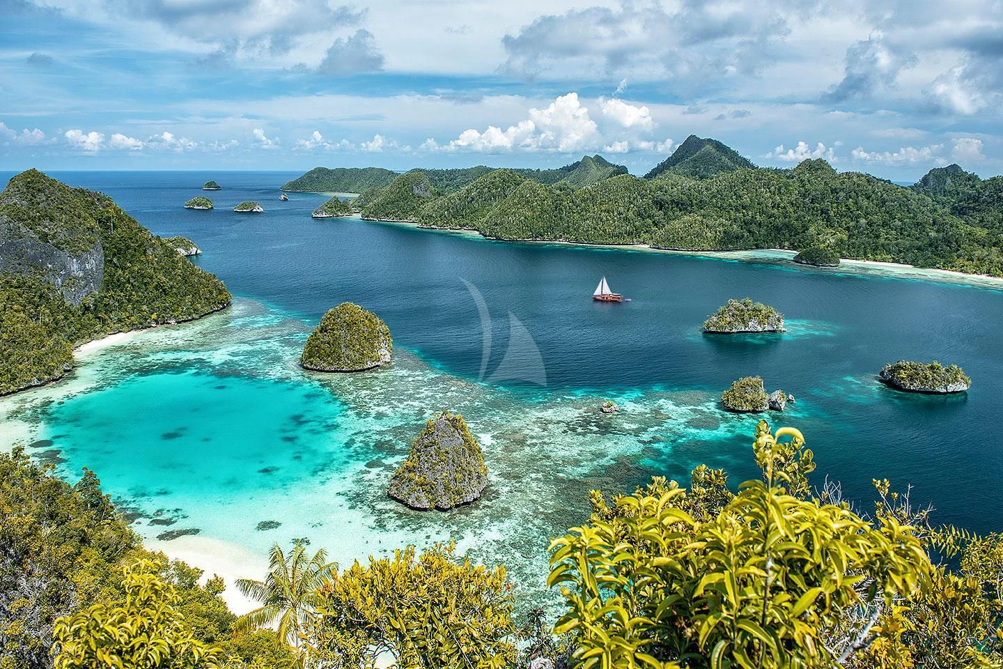 a body of water with rocks and a boat in it with Raja Ampat Islands in the background aboard SEQUOIA Yacht for Sale