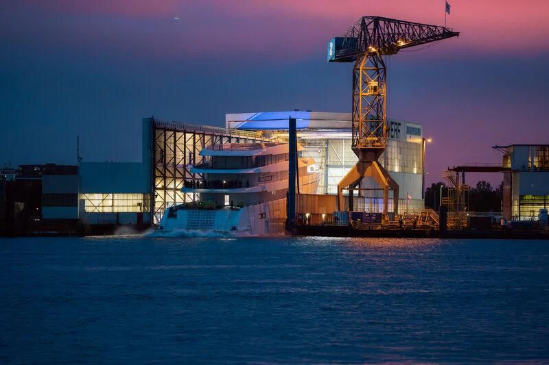 a factory with cranes and a body of water in the background aboard PI Yacht for Sale