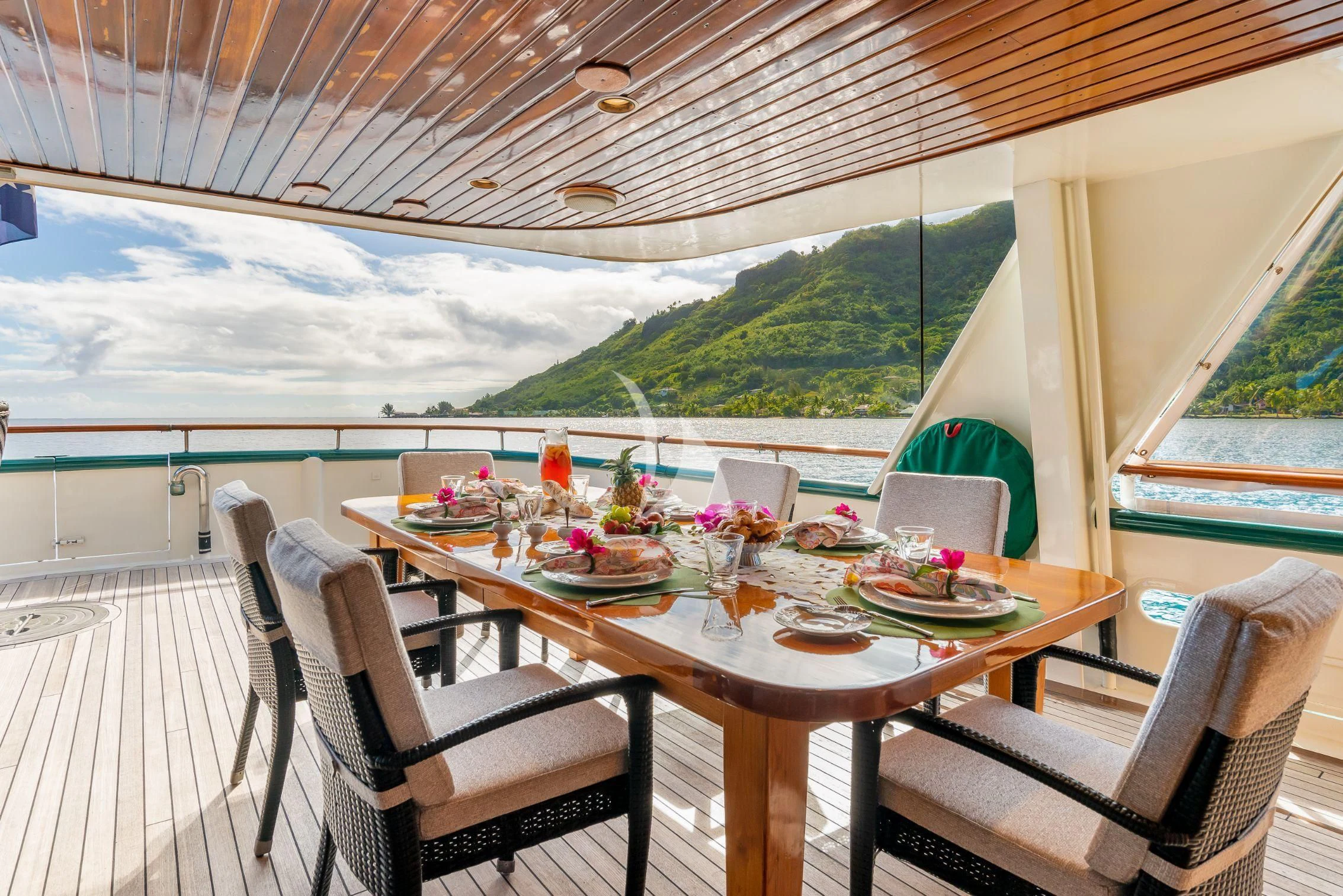 a table set for a meal on a deck with a view of the mountains and the ocean aboard ASKARI Yacht for Sale