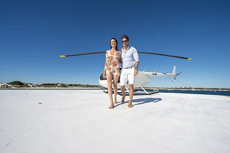 a man and woman standing on a beach with a helicopter in the background aboard CHARLEY Yacht for Sale