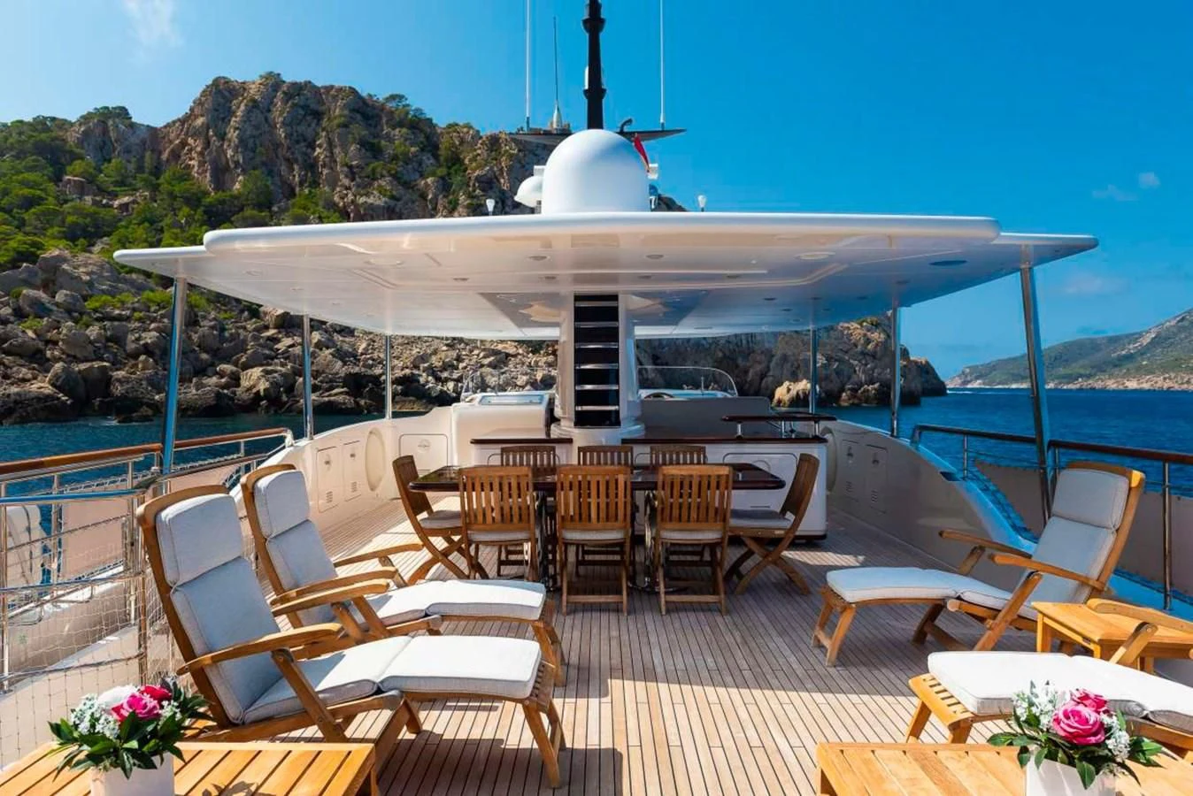 a large white building with chairs and tables on a deck with water and mountains in the background aboard LADY ALINA Yacht for Sale
