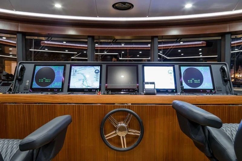 a room with many monitors and a wheel on the wall aboard VIATORIS Yacht for Sale