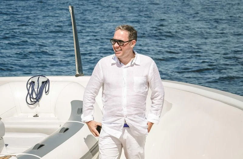 a man wearing sunglasses and a white jacket sitting on a boat aboard VIATORIS Yacht for Sale