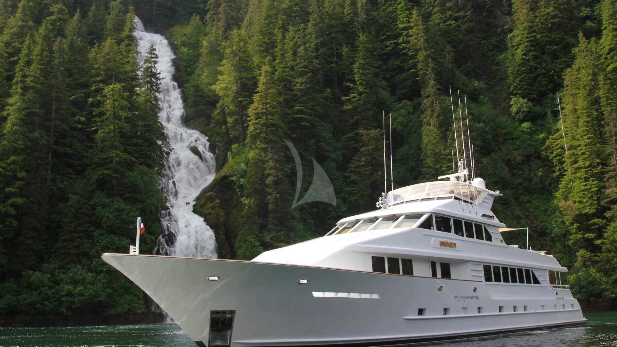 a white boat in front of a waterfall aboard SERENITY Yacht for Charter