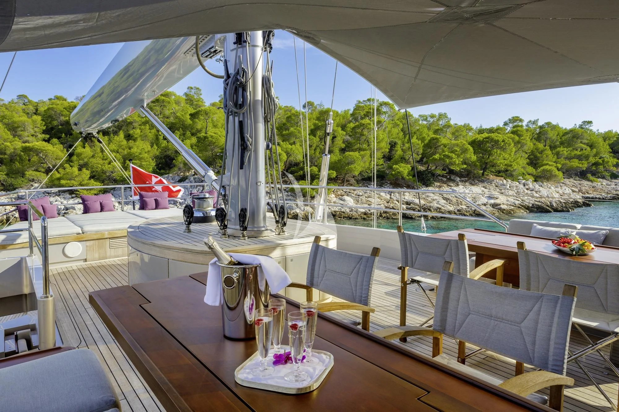 a table with chairs and a large white tent with trees and a body of water in the background aboard BARACUDA VALLETTA Yacht for Sale