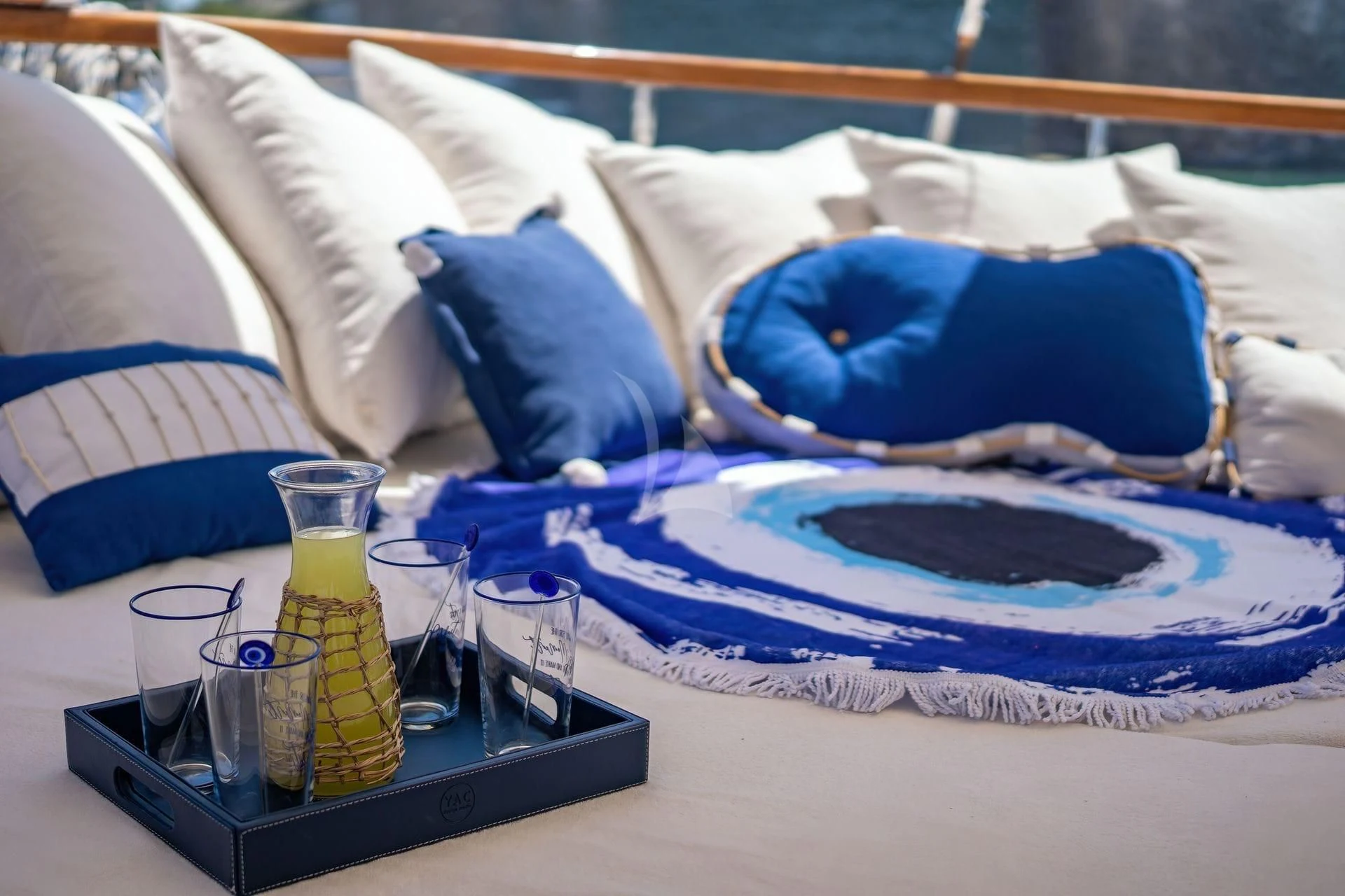 a bed with a blue and white pillow and a tray with a bottle of liquid on it aboard BABYLON Yacht for Sale