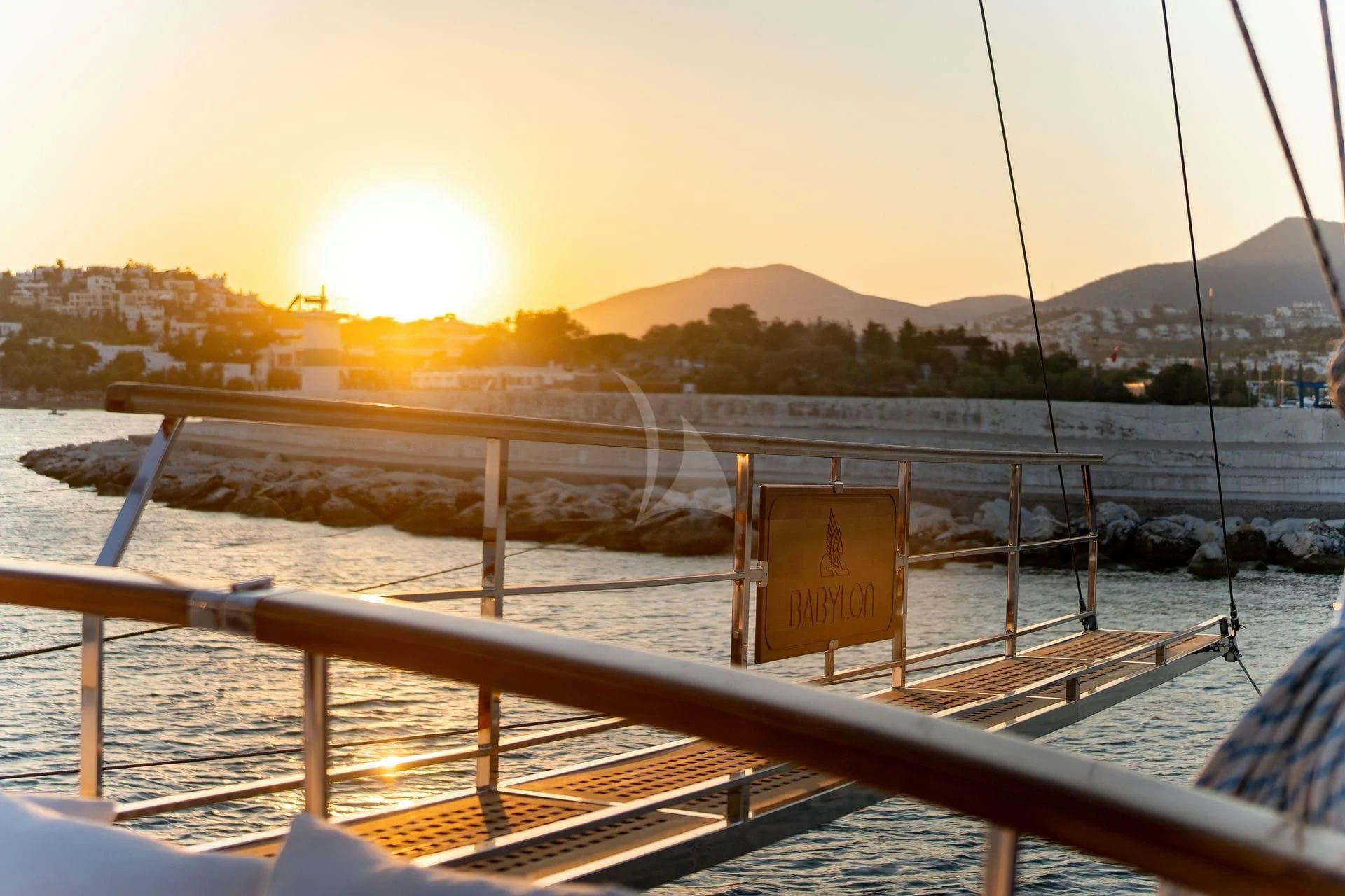 a deck with a railing and a body of water with a hill in the background aboard BABYLON Yacht for Sale