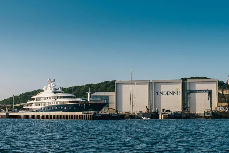 a large white ship next to a building on a dock aboard AQUILA Yacht for Sale