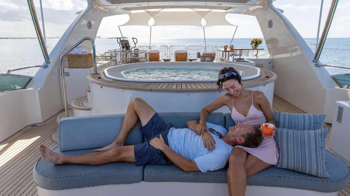 a couple of people sitting on a lounge chair on a deck with a pool and a large pool aboard NAMASTE Yacht for Sale