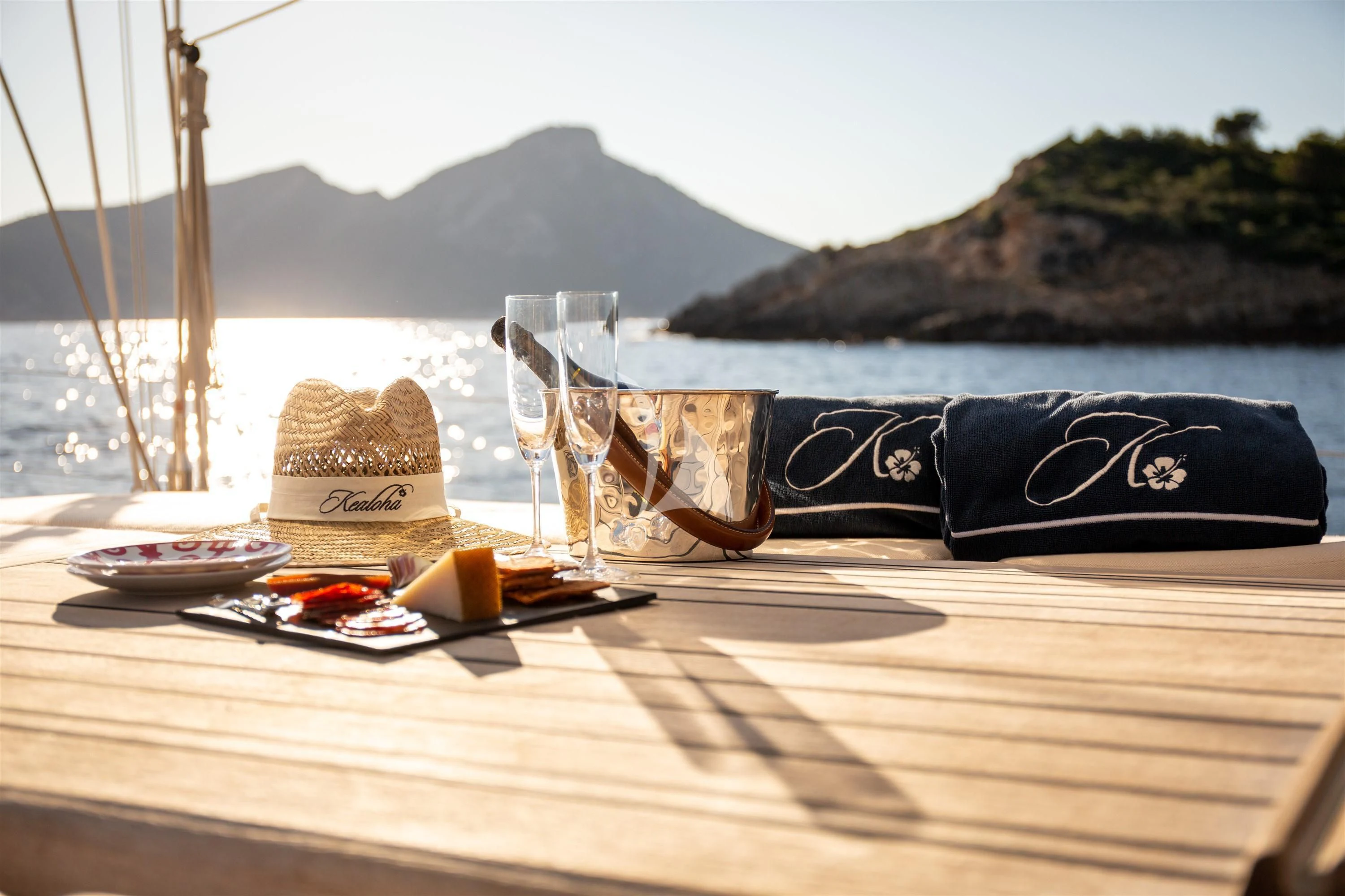 a glass of wine and a bottle on a table with a beach and water in the background aboard KEALOHA Yacht for Sale