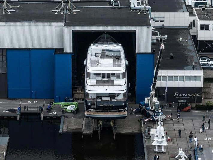 a large white vehicle with a large blue door and a group of people walking around it aboard MOONSHADOW Yacht for Sale