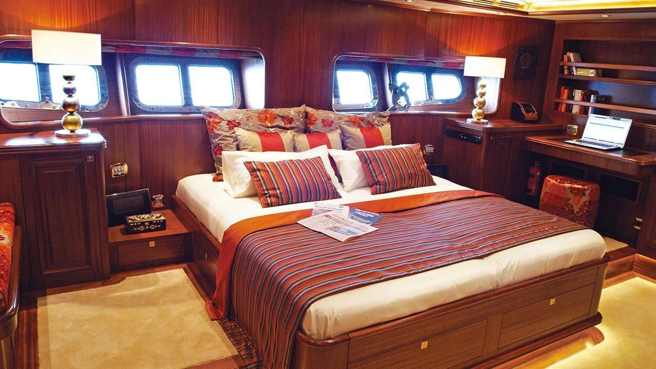 a bed with a brown comforter and pillows in a room with a window and a desk with aboard CLEAR EYES Yacht for Sale