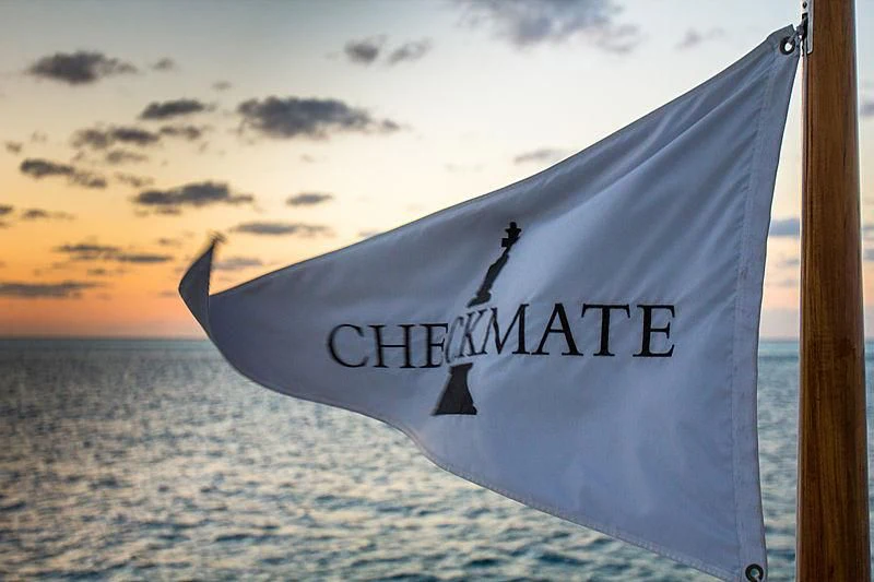 a white and black flag on a pole on a beach aboard CHECKMATE Yacht for Charter