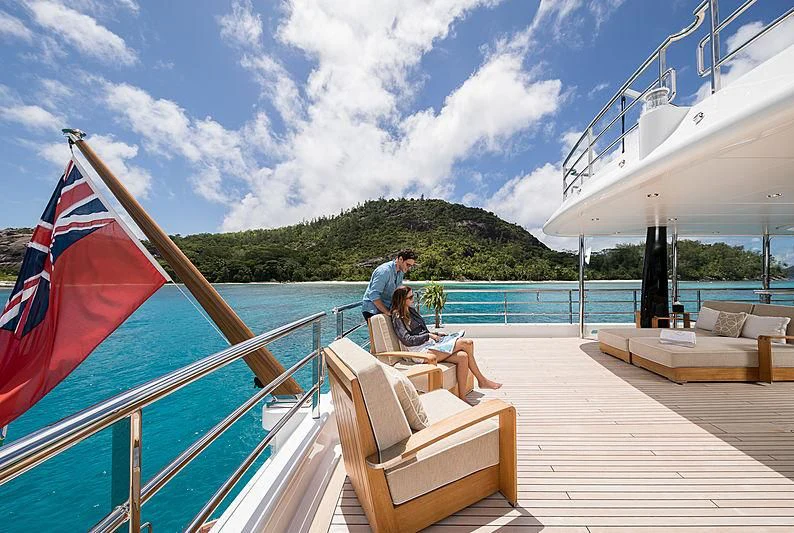 a couple sitting on a deck with a flag and a body of water in the background aboard AMIGOS Yacht for Charter
