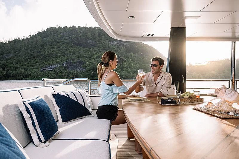 a man and a woman sitting on a boat with a table and a glass of wine aboard AMIGOS Yacht for Charter