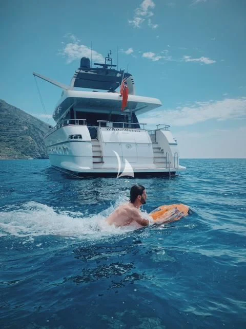a man on a surfboard in the water next to a boat aboard WHITEHAVEN Yacht for Sale