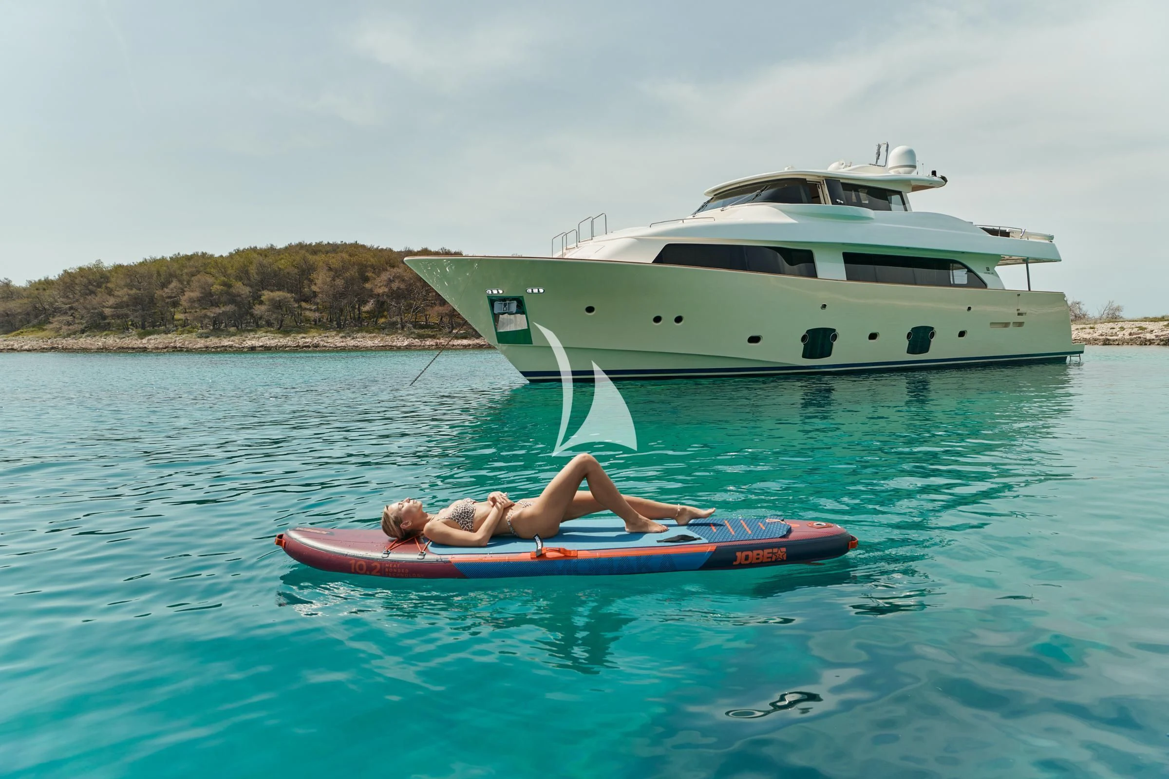 a person lying on a surfboard in the water next to a boat aboard FRIEND'S BOAT Yacht for Charter