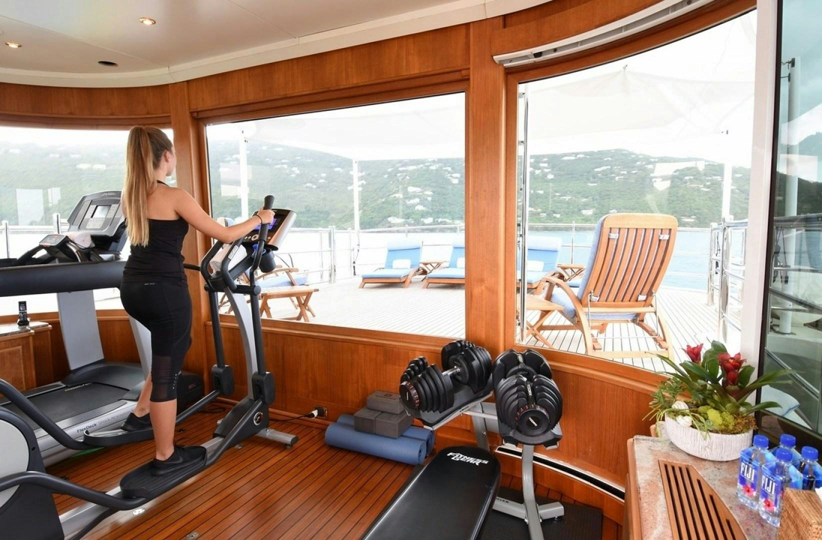 a person standing in a room with a large window and a table with chairs and a plant on aboard NEXT CHAPTER Yacht for Sale