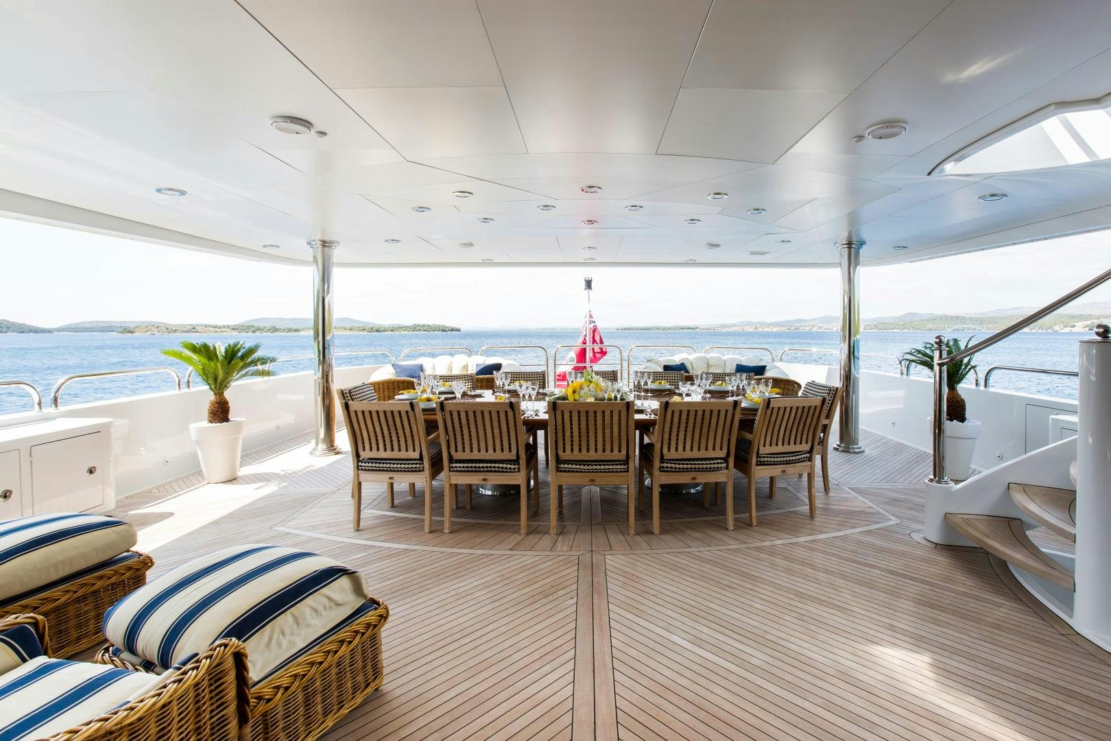 a wooden table and chairs on a deck overlooking a beach aboard MUSTIQUE Yacht for Sale