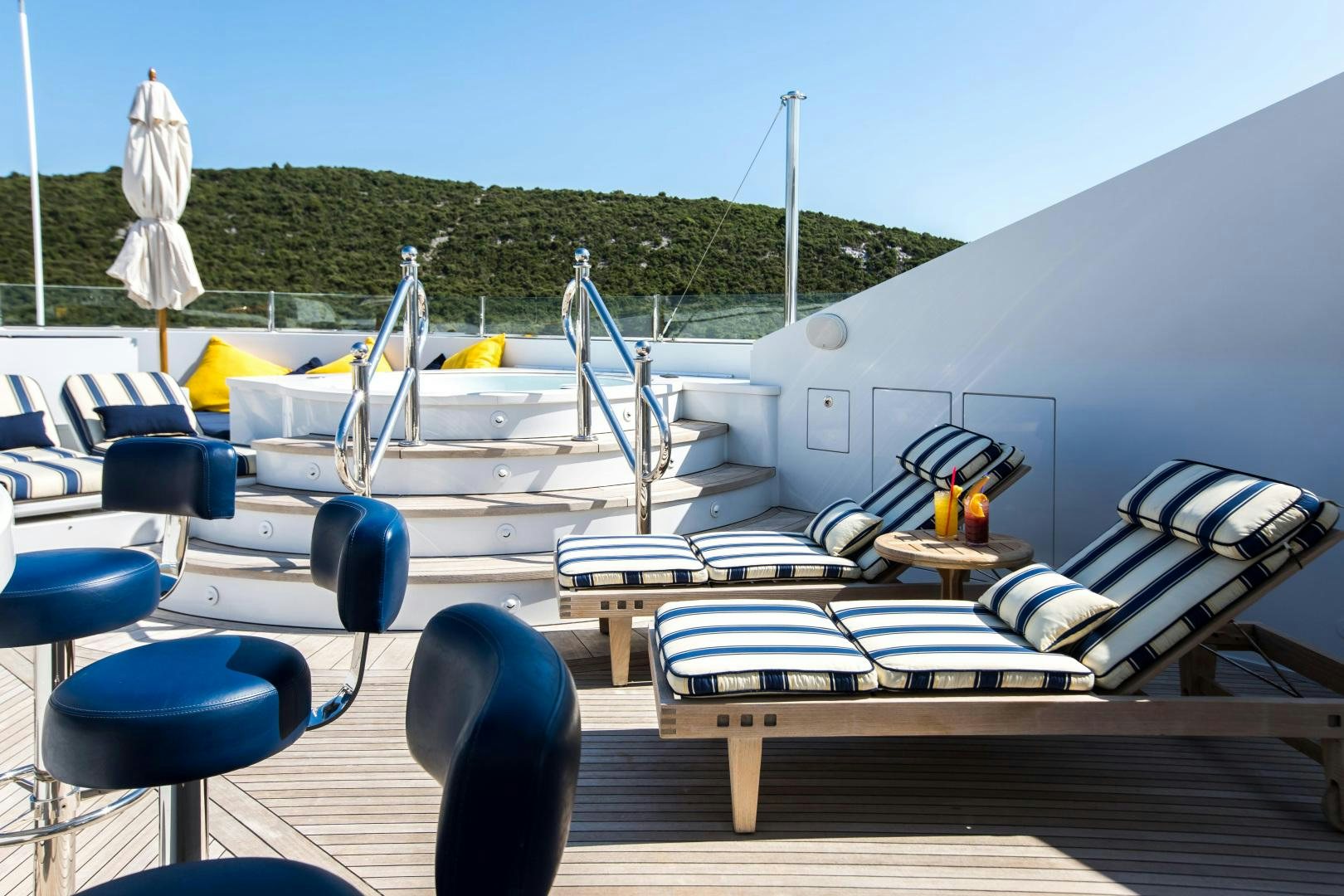 a pool with lounge chairs and a deck with a building in the background aboard MUSTIQUE Yacht for Sale