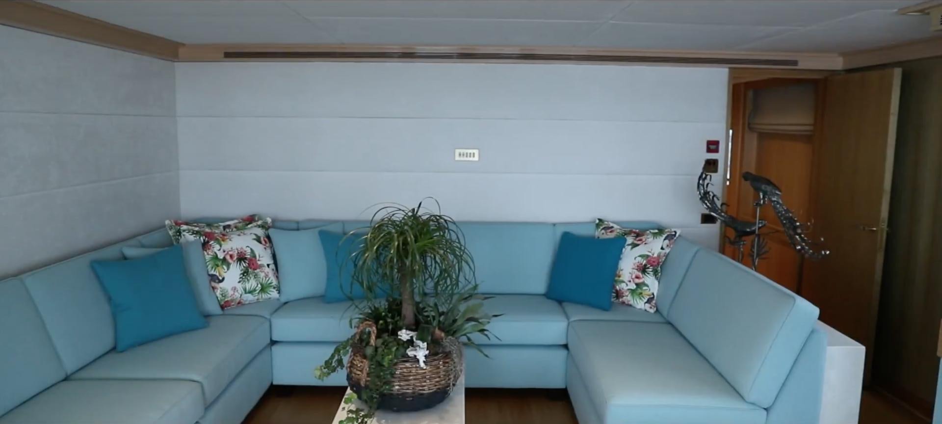a living room with a blue couch and a plant on the table aboard ANNA J Yacht for Sale