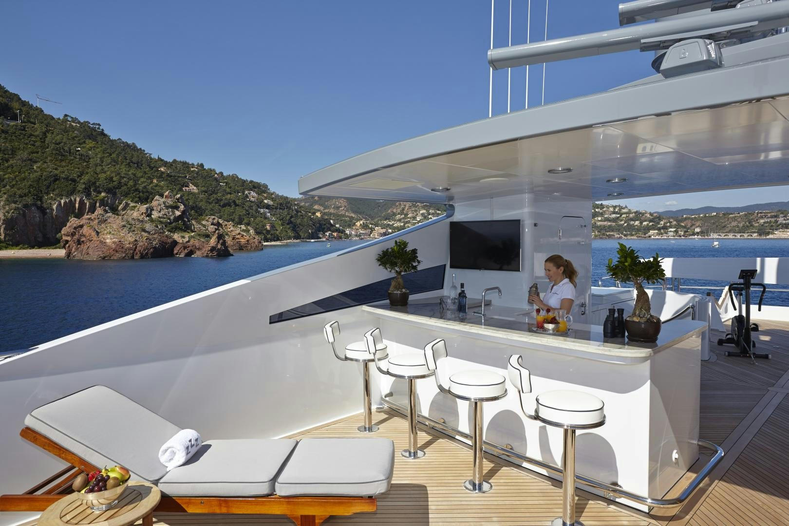 a person sitting on a chair at a table on a patio with a pool and trees and a aboard ZOOM ZOOM ZOOM Yacht for Sale