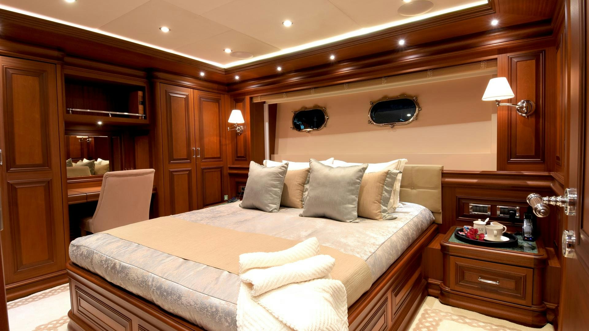 a bed with a white sheet and pillows in a room with wood cabinets aboard OMNIA Yacht for Sale