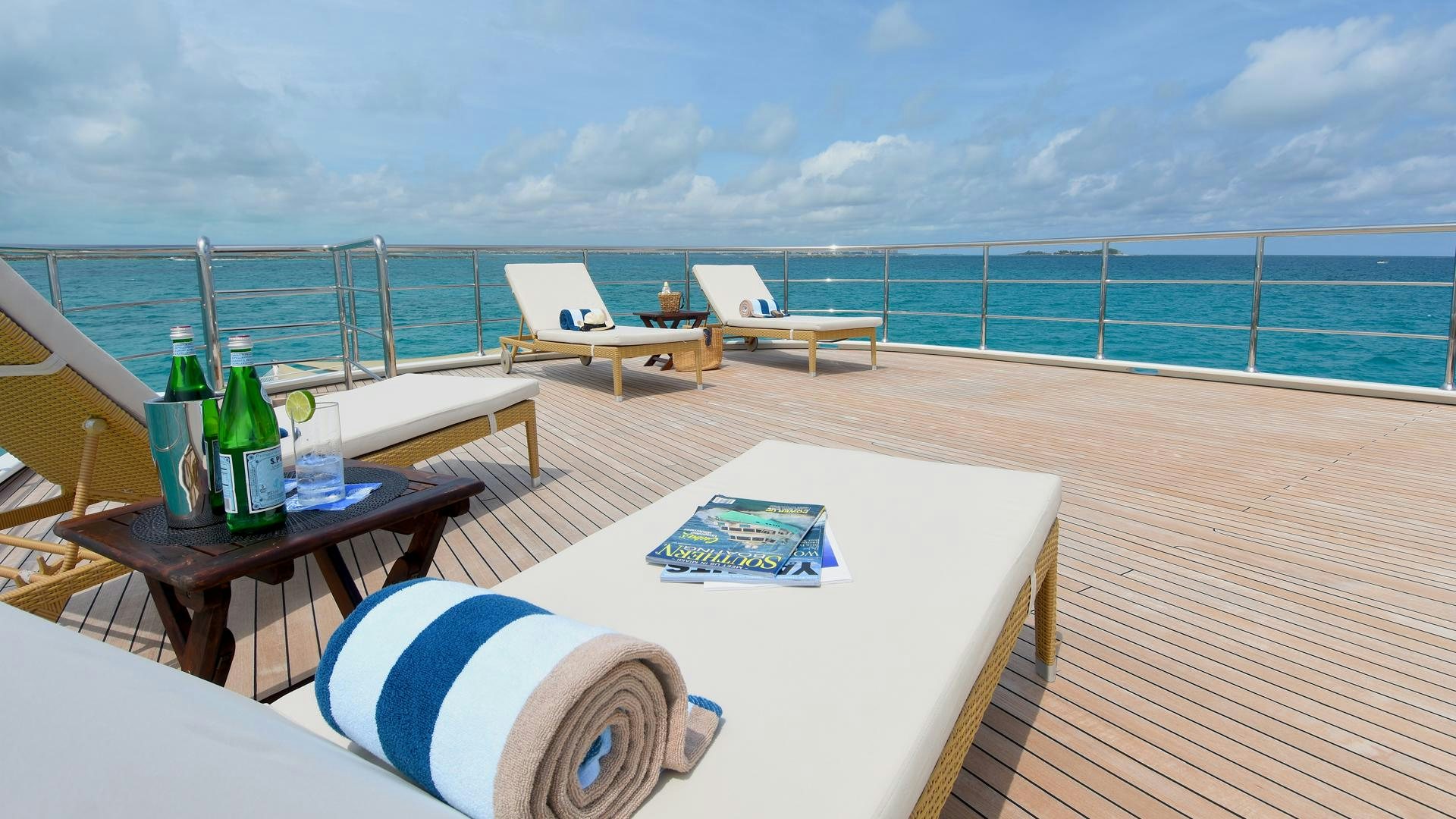 a table with chairs and bottles on it next to a body of water aboard OMNIA Yacht for Sale