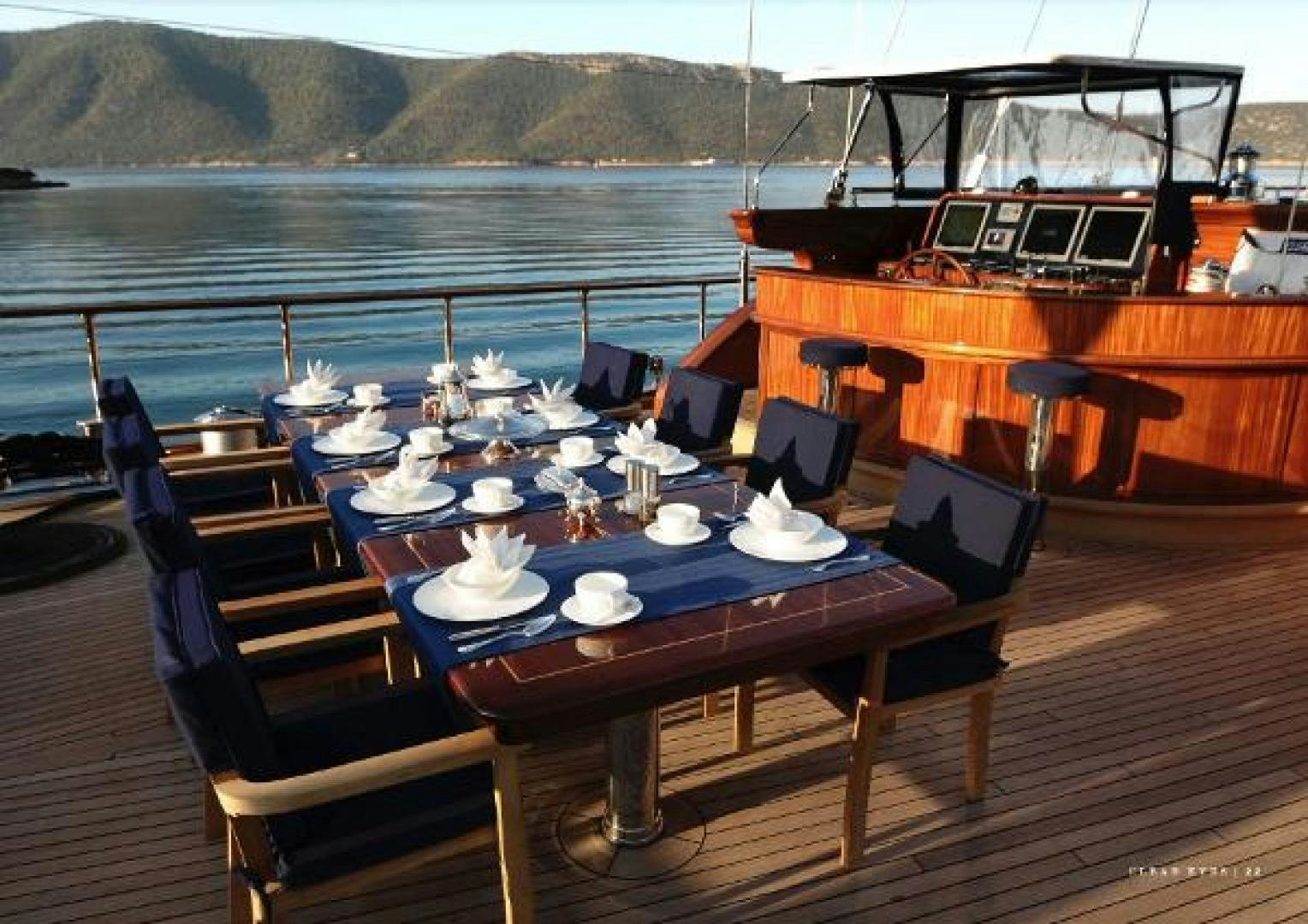 a table with plates and cups on it on a deck with a boat in the water aboard CLEAR EYES Yacht for Sale