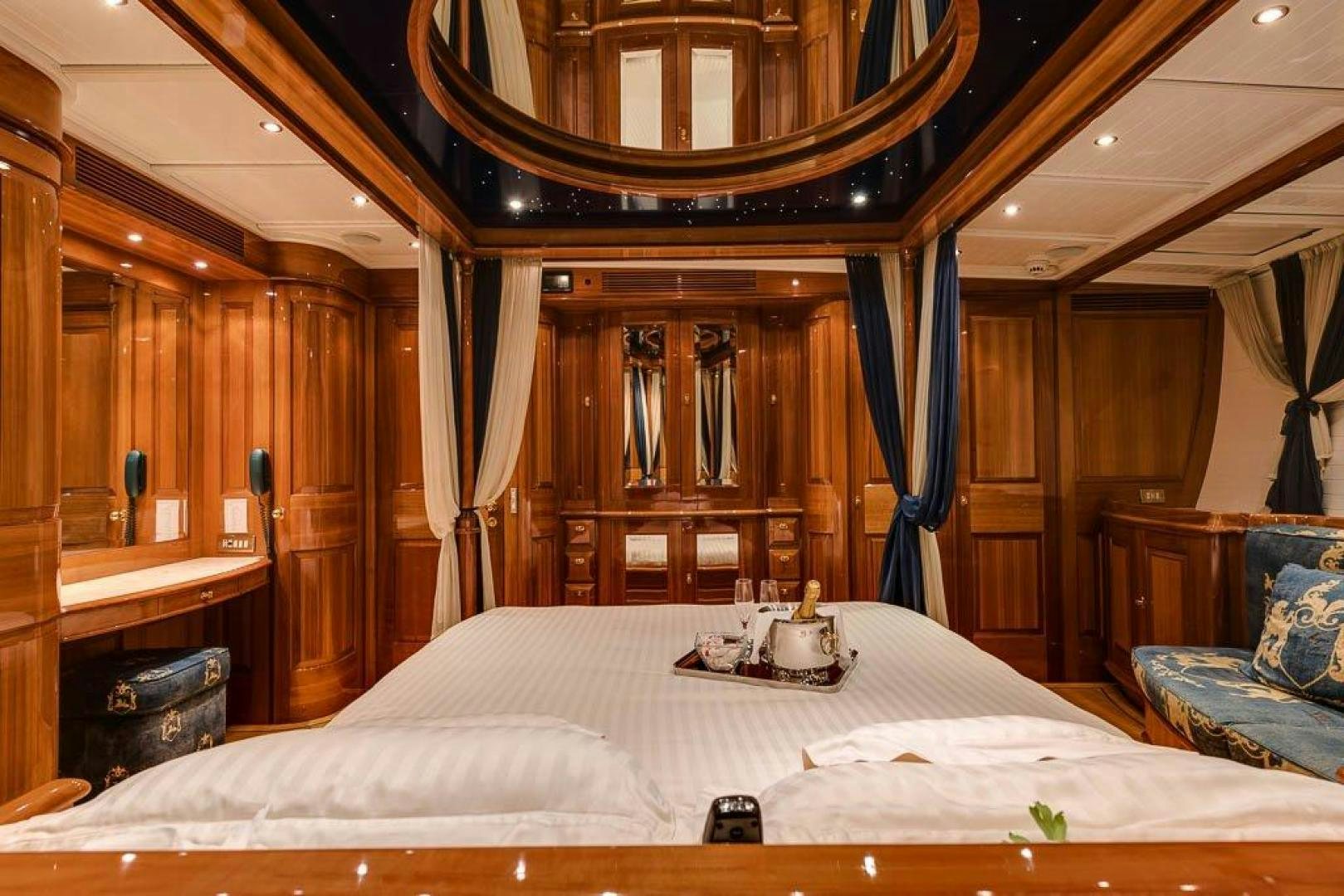 a bed with a white sheet and a table with a chair and a mirror aboard DELUSHA Yacht for Sale