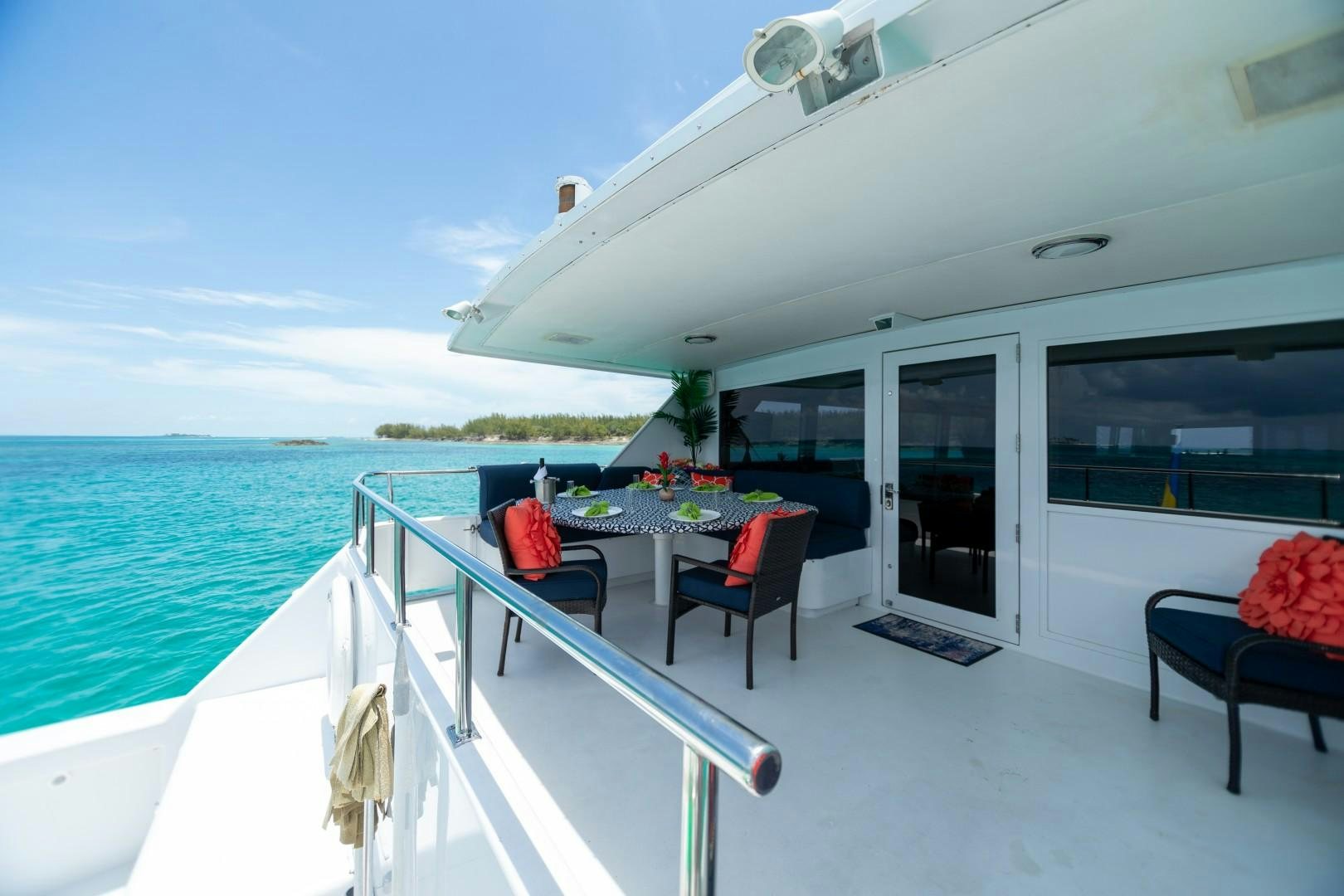 a deck with a table and chairs on it next to a body of water aboard ISLAND TIME Yacht for Sale