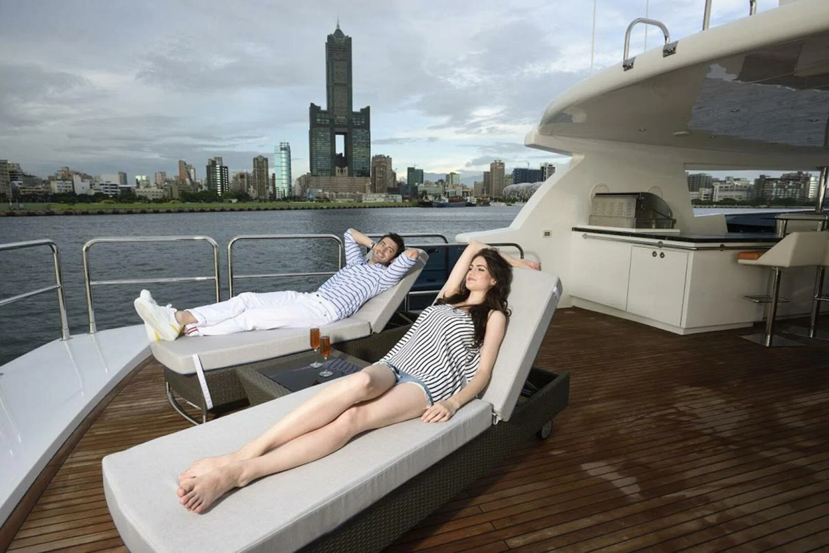 a couple sitting on a lounge chair on a deck with a city in the background aboard JOHNSON 93 OPEN FB Yacht for Sale