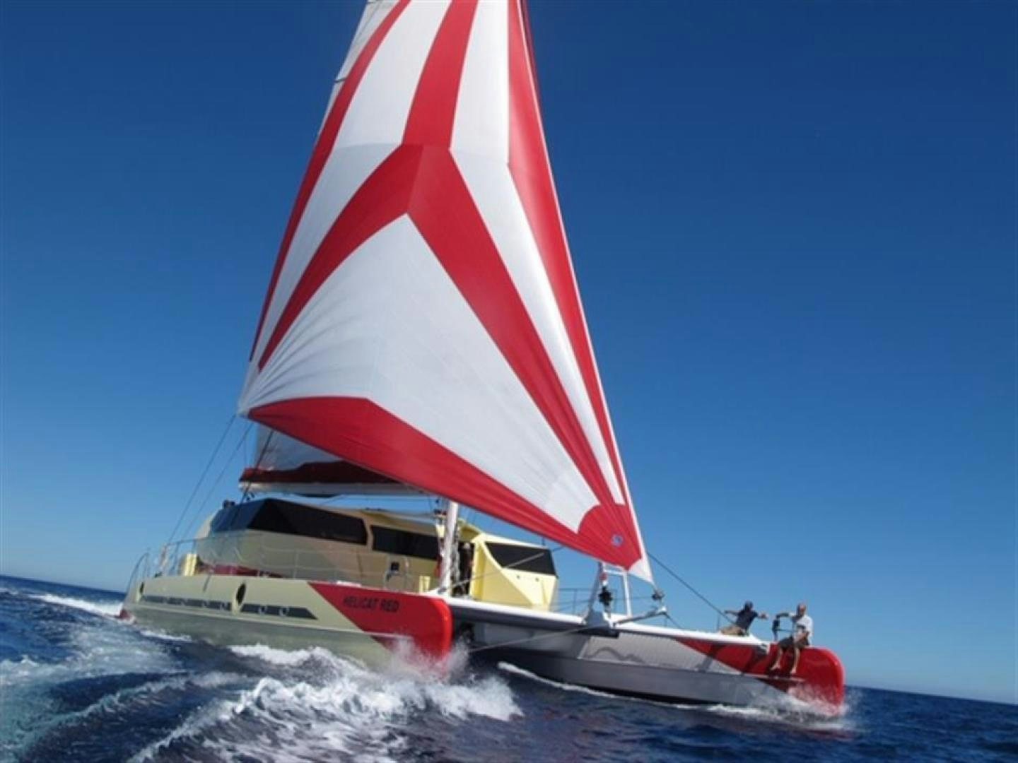 a sailboat with a red and white sail aboard HELICAT RED Yacht for Sale
