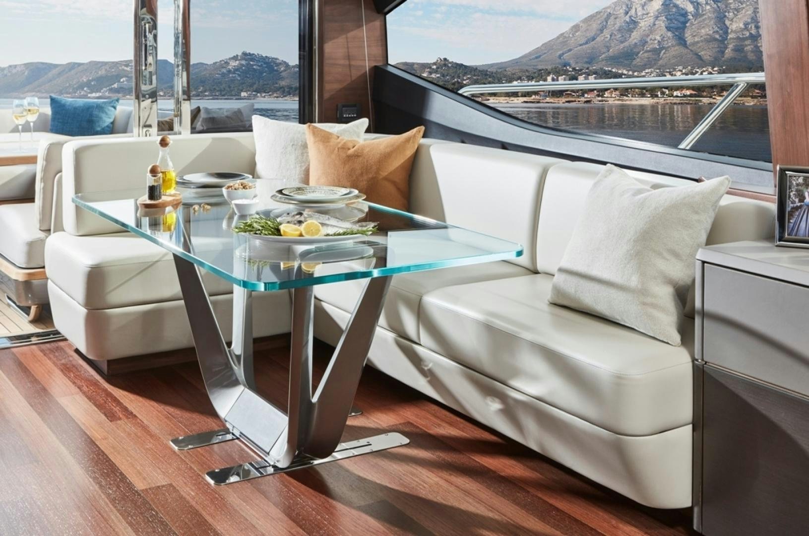 a white couch with a glass table and a white coffee table with a view of mountains and water aboard S78  Yacht for Sale