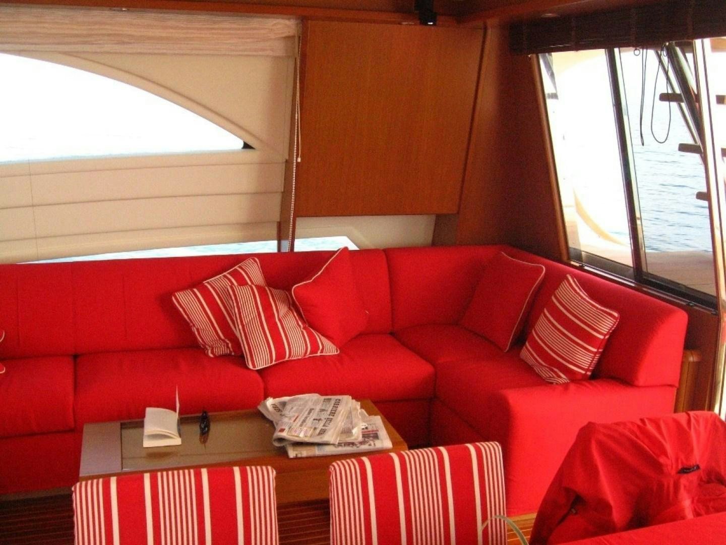 a red couch with a table and chairs in a room with windows aboard No Name Yacht for Sale