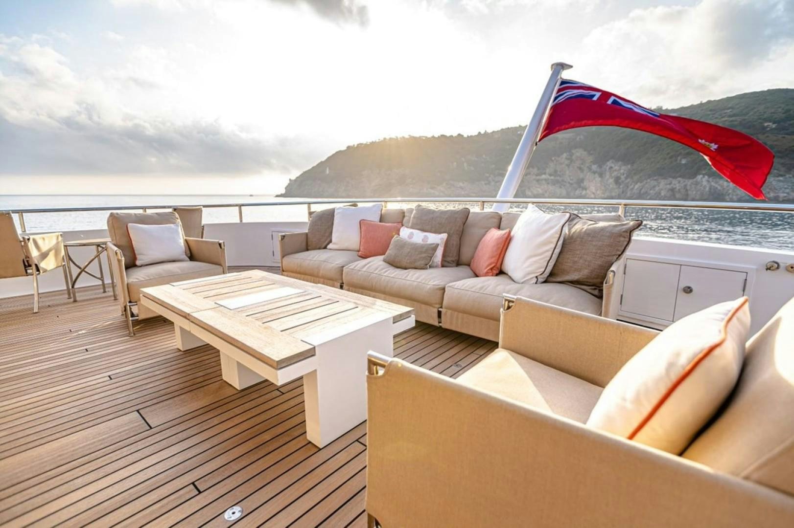 a living room with a large sofa and a table with a red umbrella aboard TASIA Yacht for Sale