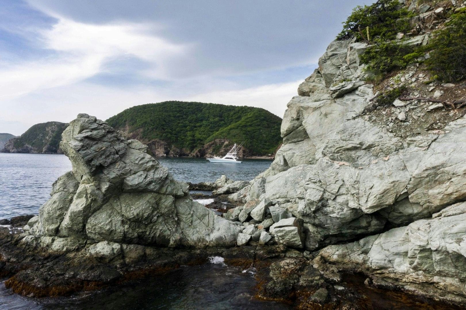 a rocky beach with a body of water and trees in the background aboard TRANQUILO Yacht for Sale