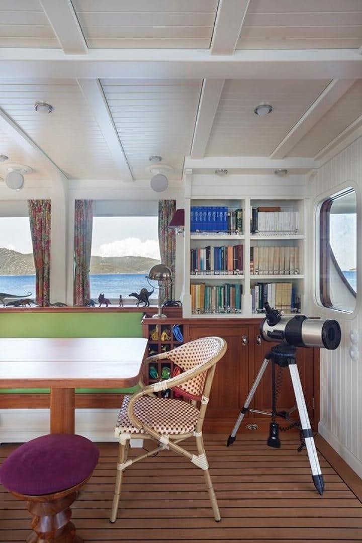 a room with a table chairs and shelves with books on the shelves aboard DARWIN Yacht for Sale