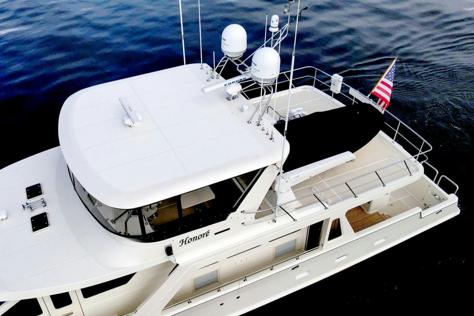 a white yacht with a flag on the front aboard HONORE Yacht for Sale