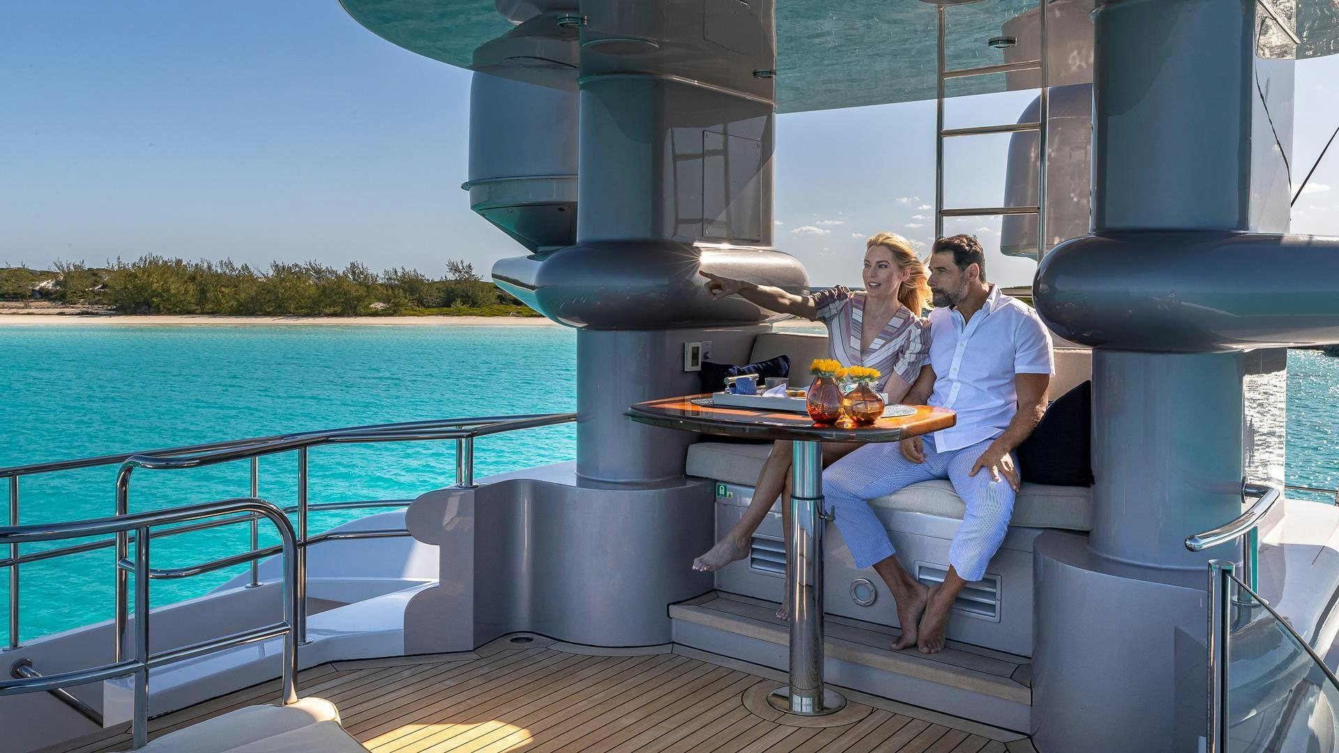 a man and woman sitting at a table with a drink and a large body of water in the aboard STARSHIP Yacht for Sale