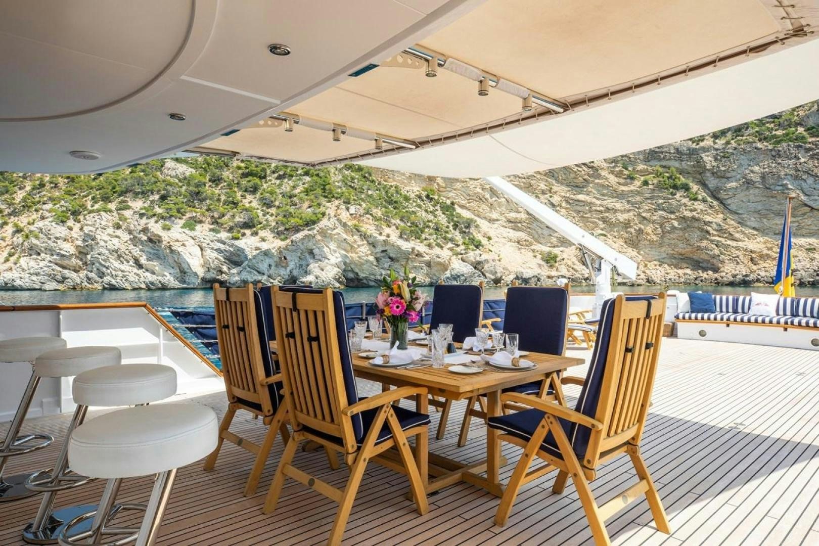 a table set for a meal on a deck overlooking a large mountain aboard MONACO Yacht for Sale