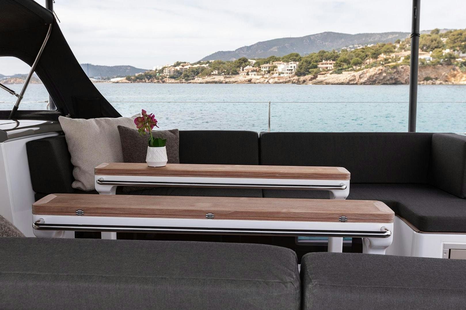 a couch and a table by a window with a body of water in the background aboard CIN CIN Yacht for Sale