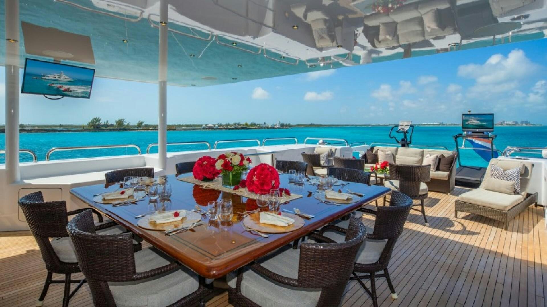 a table on a deck with chairs and a pool in the background aboard STARSHIP Yacht for Sale