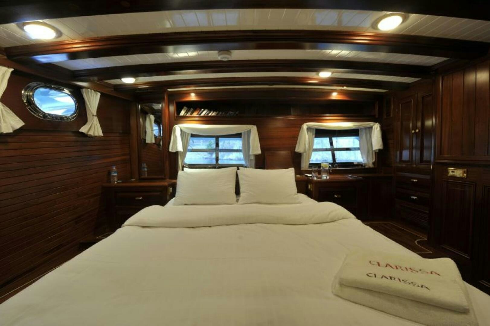 a bed with a white sheet and pillows in a room with wood cabinets aboard CLARISSA Yacht for Sale