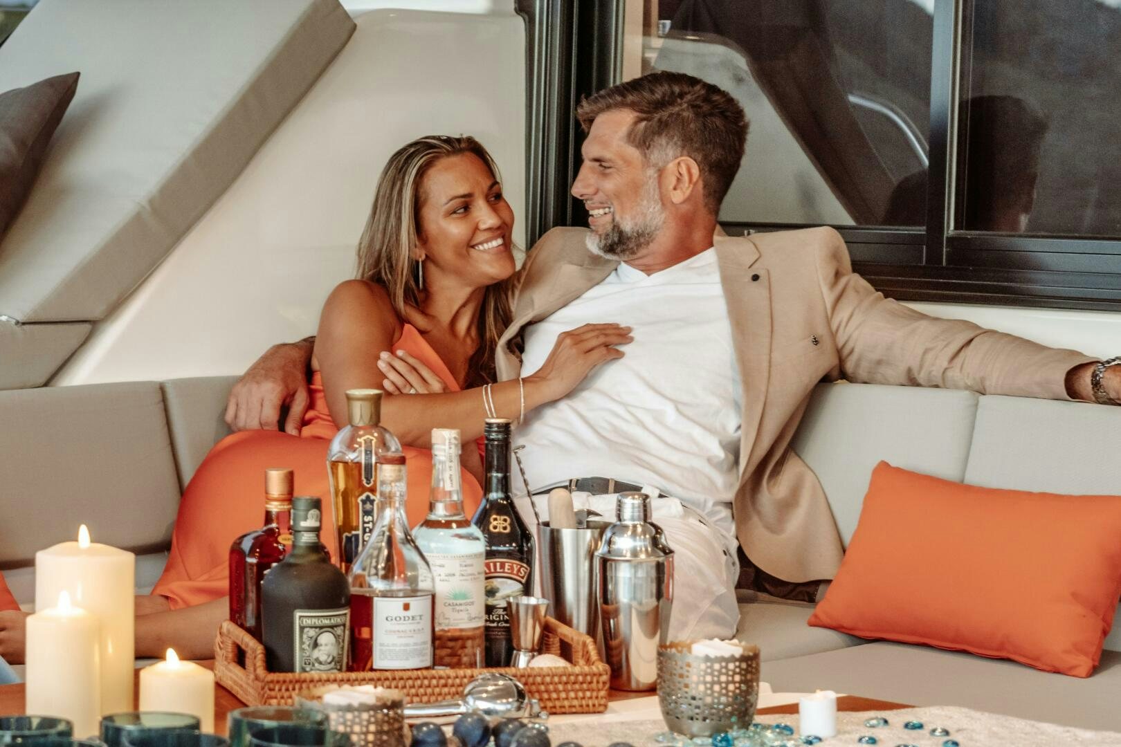 a man and woman sitting on a couch with a drink and a table with food and drinks aboard OCEANUS Yacht for Sale