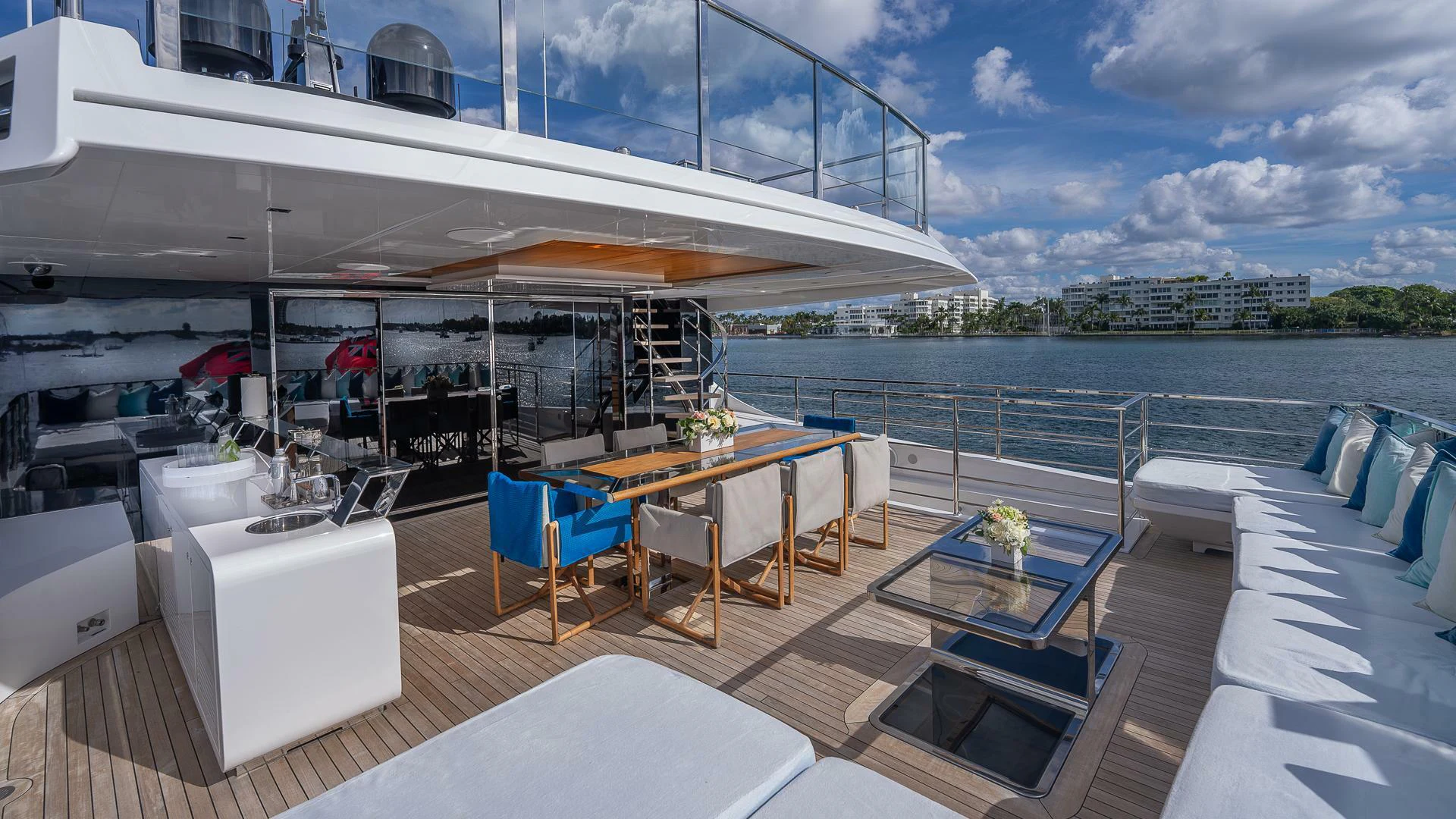 a room with a table and chairs on a deck with a view of the water and a city aboard NAMASTE Yacht for Sale