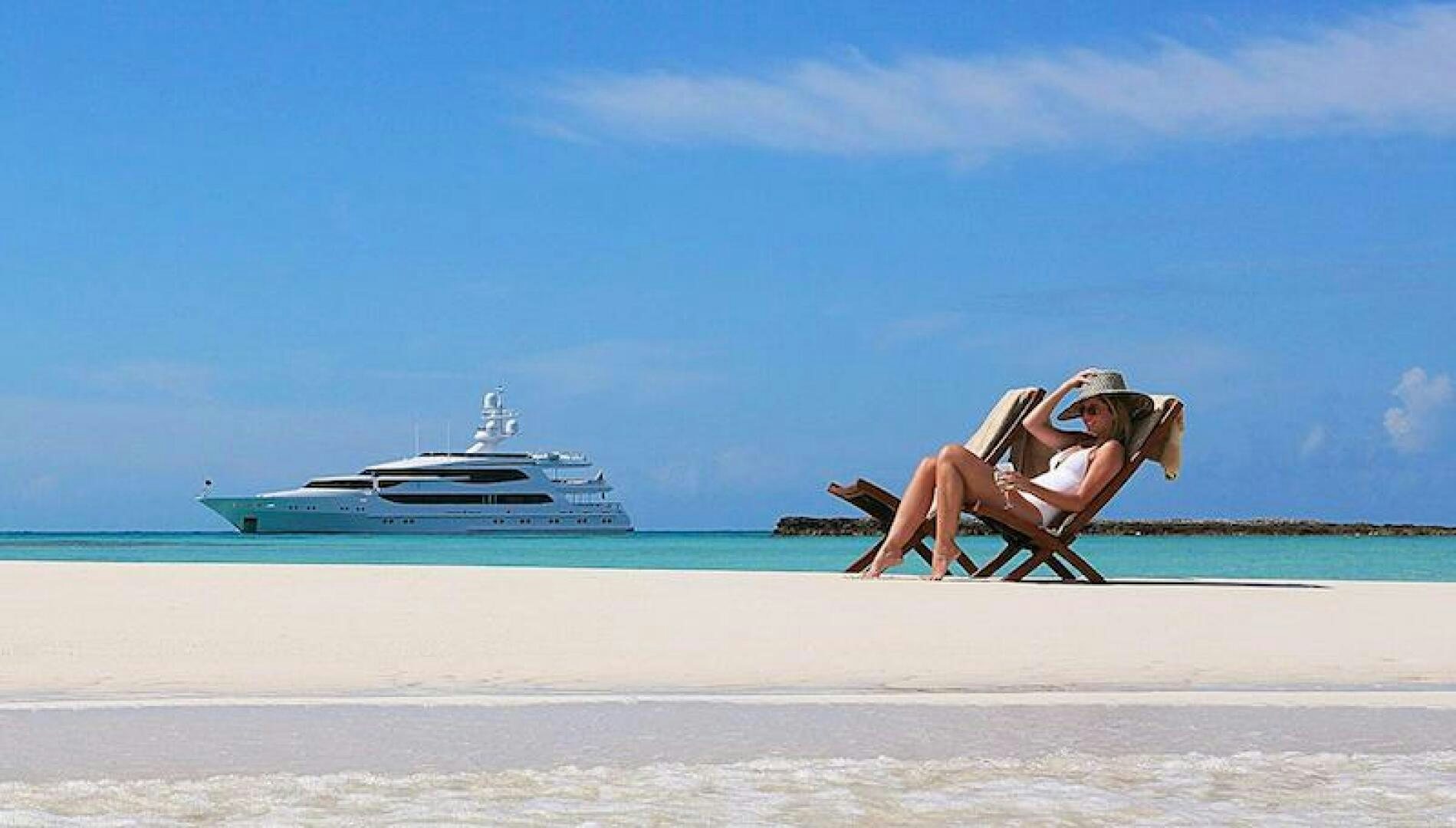 a person sitting on a beach with a boat in the background aboard JOY Yacht for Sale