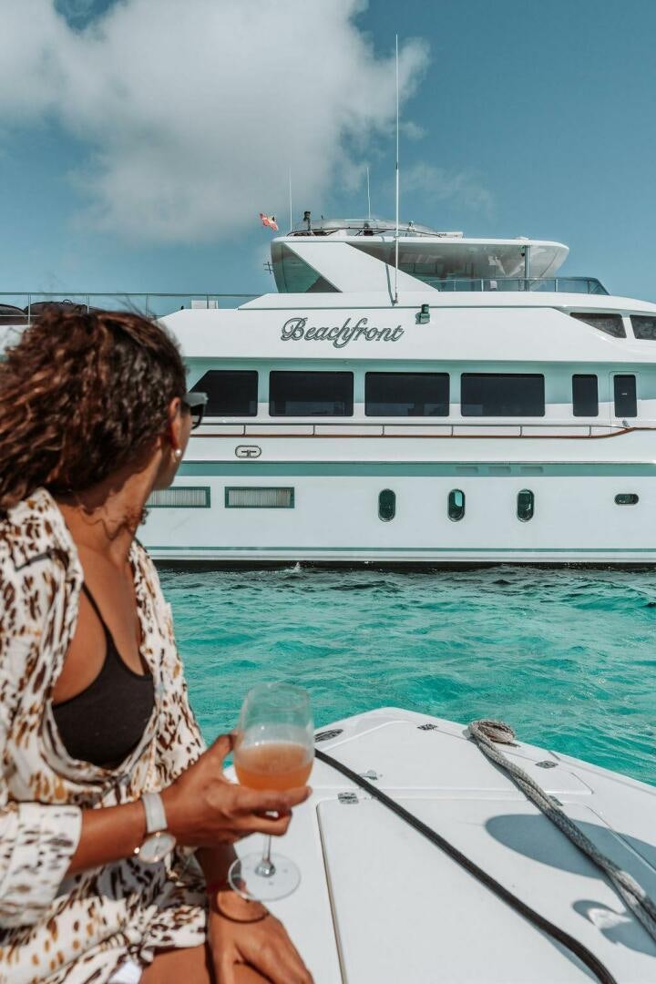 a person holding a glass of wine looking at a boat aboard BEACHFRONT Yacht for Sale